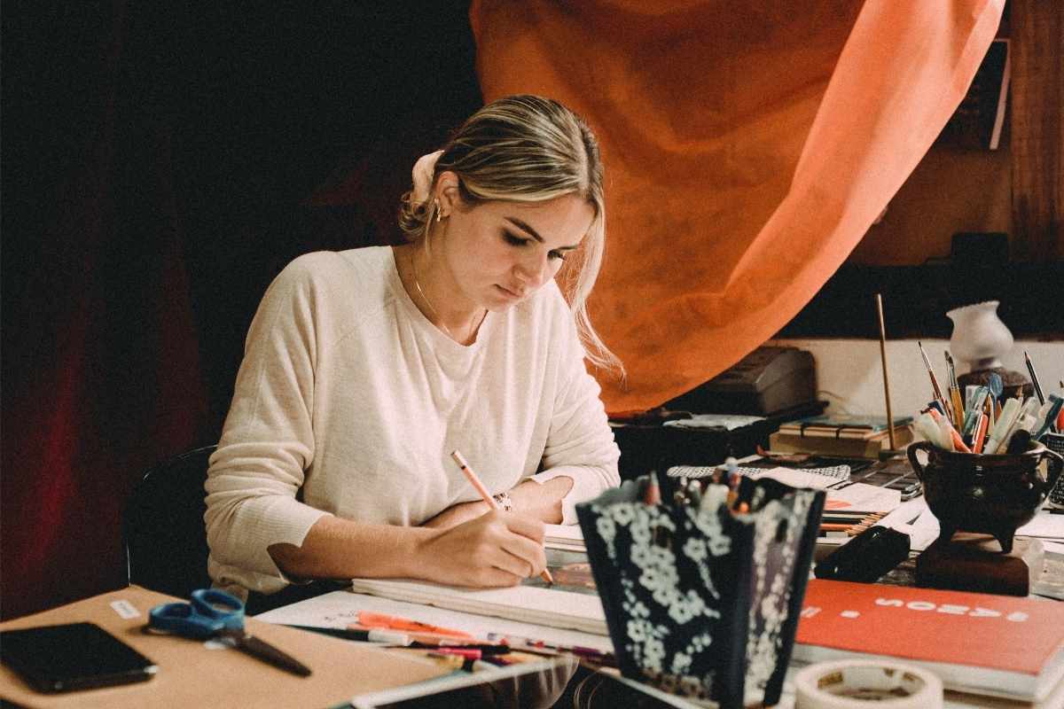 Woman in white shirt paints on a desk and explores the creative journey with Bethany Webster.