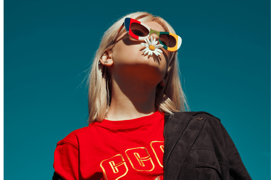 Teenager in bright sunglasses with a white flower in her mouth. Explore the importance of healing your inner teenager with Bethany Webster