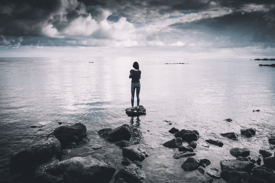 A woman stands on a rock at the edge of the ocean. Here's how to practice discernment vs judging with Bethany Webster. Photo: John Salvino