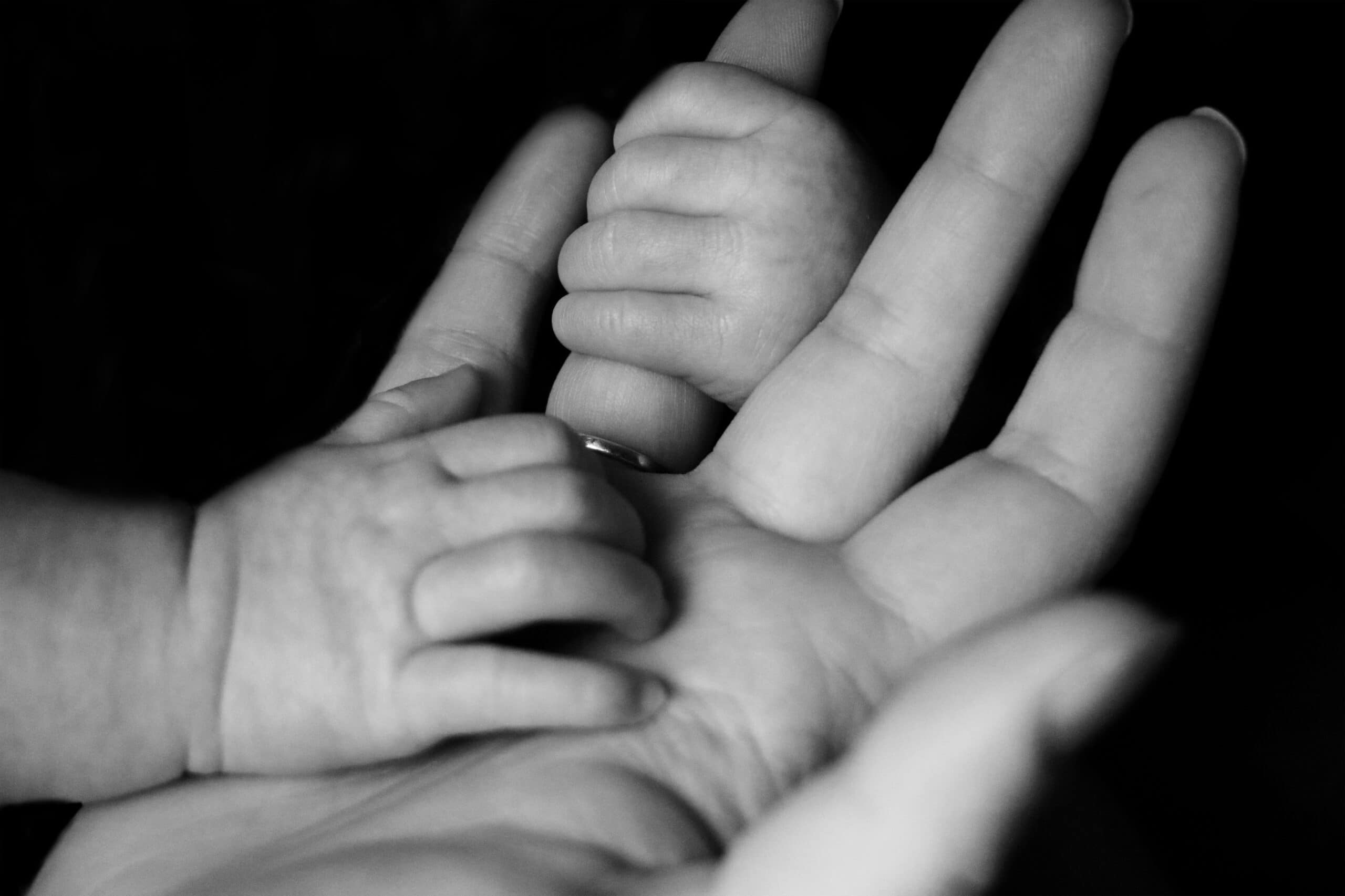 Baby's hands grasp mother's fingers in black and white Why are others abusive to daughters? Explore how your mom's inner child, trauma, and deprivation consciousness lead to a toxic relationship.